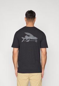 Čierne tričko s krátkym rukávom z mäkkej látky s veľkým sivým grafickým motívom ryby na chrbte, s aerodynamickým tvarom a okrúhlym výstrihom.