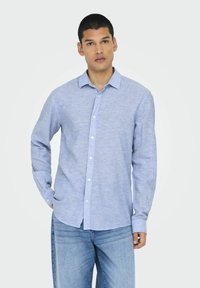 Camicia azzurra chiara con bottoni, realizzata in tessuto misto lino, con colletto, maniche lunghe e bottoni bianchi.