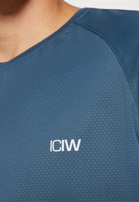 Maglietta atletica blu navy con un motivo testurizzato, scollatura rotonda e logo "ICIW" in bianco sul lato anteriore vicino alla scollatura.