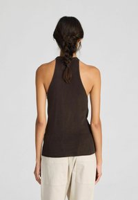 Top marrone senza maniche con scollatura alta e trama a coste, presenta una silhouette aderente, abbinato a pantaloni chiari e larghi.