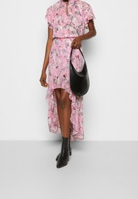Vestido floral rosa con mangas acampanadas, con un dobladillo asimétrico. Combinado con un bolso negro de hombro ybotas negras hasta el tobillo. Tejido suave con una textura lisa.