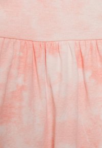 Um tecido de algodão cor pêssego apresenta um padrão tie-dye com variações subtis. A saia tem uma costura franzida para adicionar textura.