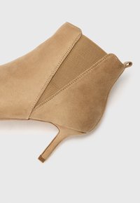 Beige nubuk nilon dengan ujung runcing, panel elastis, dan tumit stiletto setinggi 5 cm. Tekstur halus dengan desain minimalis.