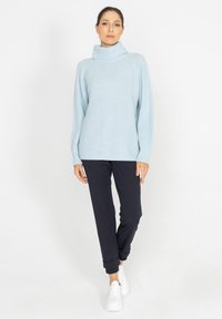 Jasnoniebieski, rypsowy sweter z wysokim kołnierzem zestawiony z granatowymi spodniami typu tapered i białymi sneakerami; luźny krój, długie rękawy, prosty design.