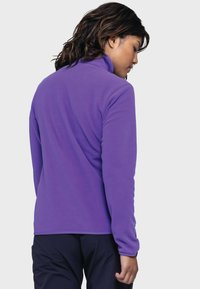 Lila Fleece-Pullover mit hohem Kragen, weicher Textur und langen Ärmeln. Besitzt ein tailliertes Design und eine saubere, nahtlose Optik auf der Rückseite.