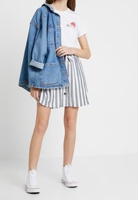 Jeansjacka, vit t-shirt med röd grafik och grå randig kjol med knappdetalj. Kompletteras med vita högskurna sneakers.