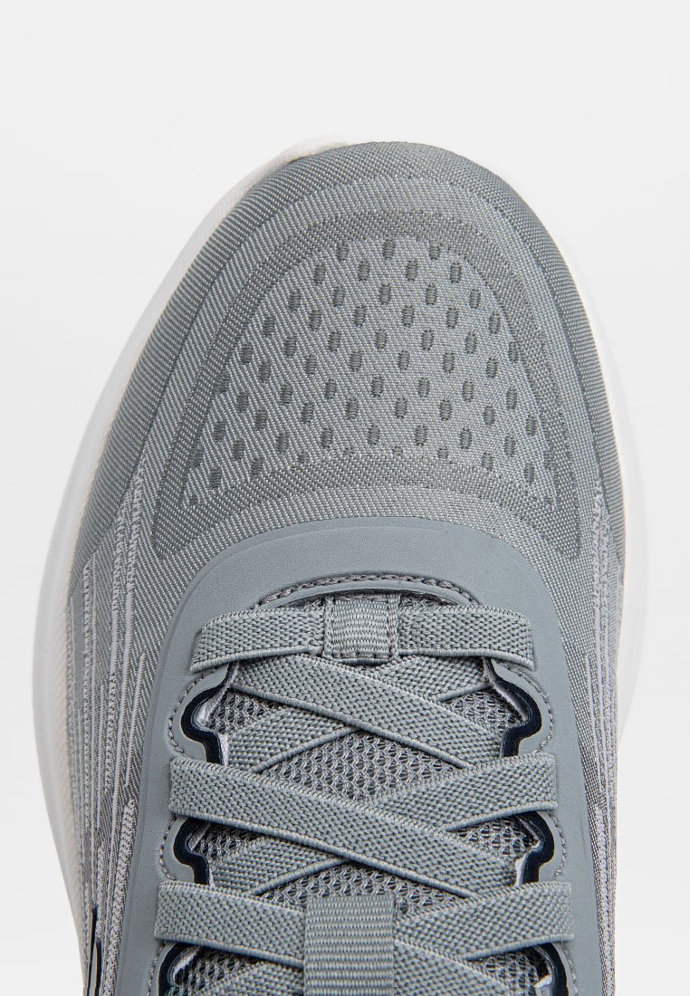 Scarpa da atletica grigia con parte superiore in rete testurizzata, linguetta imbottita e lacci. Presenta aree ventilate e una suola in gomma bianca.