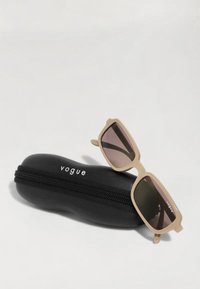 Bežasti pravokotni sončna očala z gradientnimi lečami, ki počivajo na črni zadrgi torbici z belim napisom "vogue".