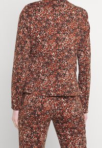 Flerfärgad kavaj och byxor i röd, svart och vit leopardmönster. Slät tyg med en figursydd design och långa ärmar.