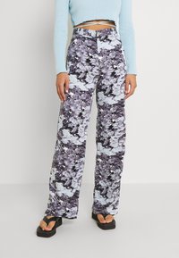 Spodnie o wysokim stanie, szerokiej nogawce w kolorowym, abstrakcyjnym wzorze fioletowym i niebieskim z białymi akcentami. Wykonane z miękkiego, teksturowanego materiału.