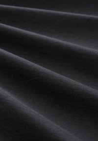 Tessuto di cotone nero con una texture morbida, caratterizzato da sottili pieghe e una superficie liscia, che presenta diverse tonalità di grigio scuro.