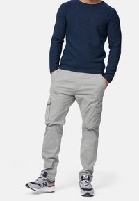 Granatowy sweter z dzianiny, szare spodnie cargo z bocznymi kieszeniami oraz sportowe buty w wielokolorowym wzorze. Luźny strój dla swobodnych okazji.