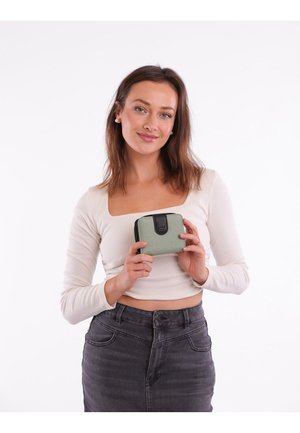 Green leather zippered wallet with a textured surface, black hardware, and a compact rectangular shape, held by a person in a light top.