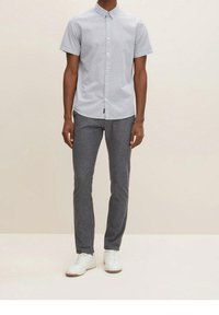 Camicia azzurro chiaro a maniche corte con un piccolo motivo a pois, abbinata a pantaloni slim-fit grigio scuro e sneakers bianche.