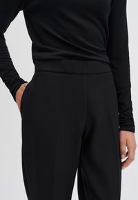 Zwarte lange mouwen top met een getailleerde pasvorm, gecombineerd met hoog ingezette zwarte broek met een gladde textuur en zijzakken.