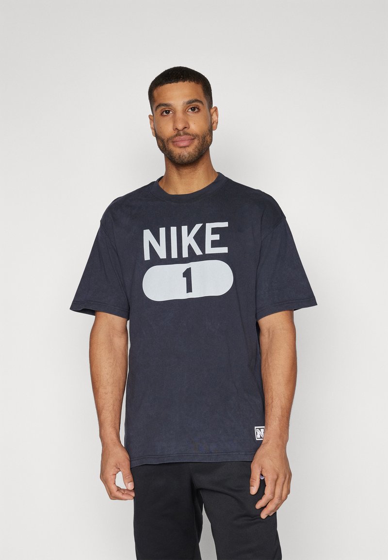 Mørkeblå bomulds t-shirt med et stort hvidt "NIKE" logo og "1" grafik på fronten. Rund halsudskæring, korte ærmer, afslappet pasform.