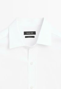 Camicia bianca in cotone con colletto classico, chiusura con bottoni e una superficie liscia. Presenta etichette del marchio in nero.