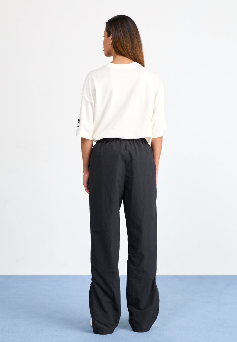 Weißes, oversized T-Shirt mit kurzen Ärmeln, kombiniert mit lockeren, schwarzen Hosen mit elastischem Bund und strukturierter Stoff.