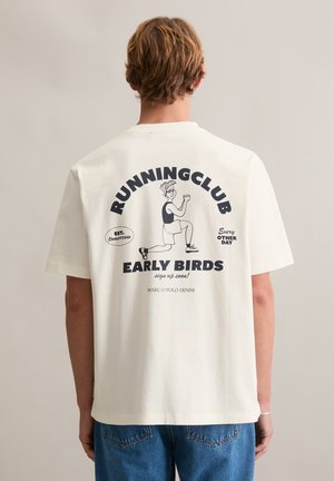 Biała bawełniana koszulka z okrągłym dekoltem, z nadrukiem graficznym przedstawiającym kreskówkowego biegacza oraz tekstem: „RUNNINGCLUB EARLY BIRDS” w kolorze granatowym.