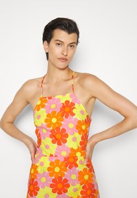 Top halter colorido com grandes padrões de flores em rosa, laranja e amarelo sobre um fundo rosa claro. As alças são finas e ajustáveis.