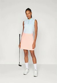 Šviesiai mėlyna be rankovių polo marškinėliai su dryžuotu raštu ir sagų užsegimu, derinami su persikų spalvos sijonu. Baltos sportinės bateliai ir kojinės papildo aprangą.