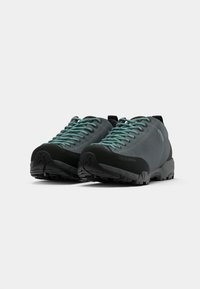Sapatos de caminhada cinzentos com solas de borracha pretas, parte superior texturizada e atacadores em teal. Apresentam uma biqueira reforçada e uma aba na parte traseira para facilitar o calçar.
