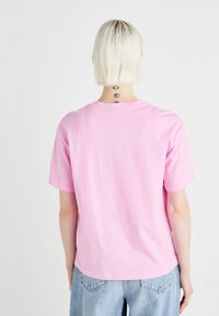 Růžové bavlněné tričko s krátkým rukávem, s kulatým výstřihem a volným střihem, zobrazené zezadu.