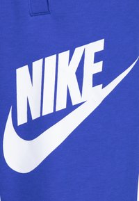 Modra bombažna športna majica z velikim belim logotipom Nike in dizajnom kljukice, gladka tekstura in izrazite podrobnosti blagovne znamke.