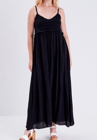 Robe maxi noire avec un corsage en crochet, des bretelles spaghetti et une jupe fluide. Elle présente une coupe ample et une texture subtile.