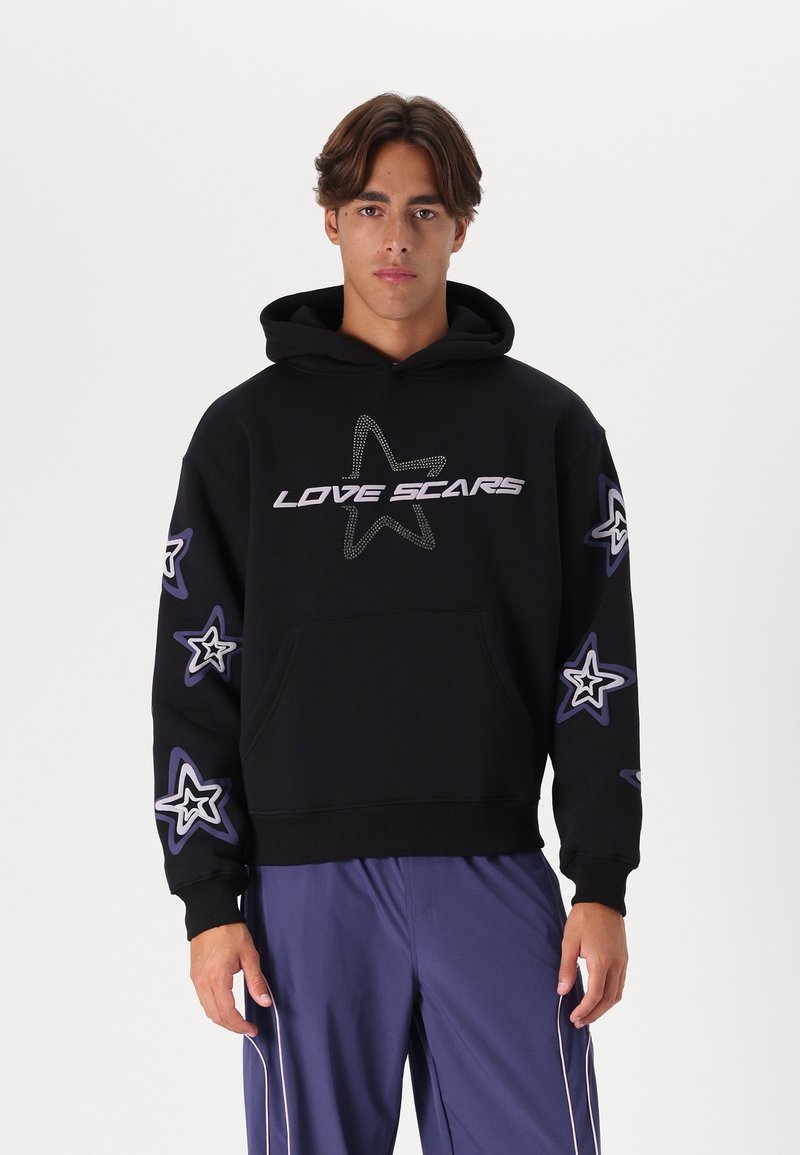 Sort hættetrøje med teksten "LOVE SCARS" i sølv, med stjerne designs i blå og hvid langs ærmerne. Blendet stof af bomuld, kængurulomme.