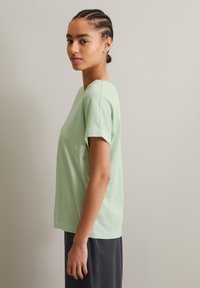 Hellgrünes Kurzarm-Cotton-T-Shirt mit lockerer Passform und rundem Halsausschnitt, getragen zu dunklen Hosen. Zugehörige glatte Textur, keine Muster.