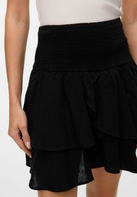 Sorte, lagdelte skjørt med smock midje, laget av myk, lett stoff med volanglag. Nederkanten er litt ujevn.