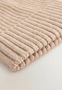 Strickstoff in Beige mit vertikalen Rippen, der Textur und eine weiche Oberfläche zeigt. Gerollter Rand sichtbar, mit subtilen Farbvariationen.