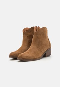 Botas de tobillo de ante marrón con puntera redondeada, cremallera lateral y tacón bajo de bloque. Presenta costuras decorativas a lo largo de los bordes superiores.