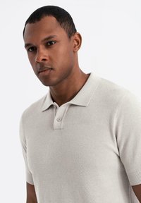 Beige pikétröja med ett strukturerat mönster, korta ärmar och en tvåknapplåsning. Slät tygkvalitet med subtil stretch och klassisk passform.