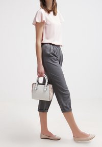 Ljusrosa kortärmad blus, grå cropped byxor, beiga ballerinaskor och en liten tvåfärgad handväska med en strukturerad design och handtag upptill.