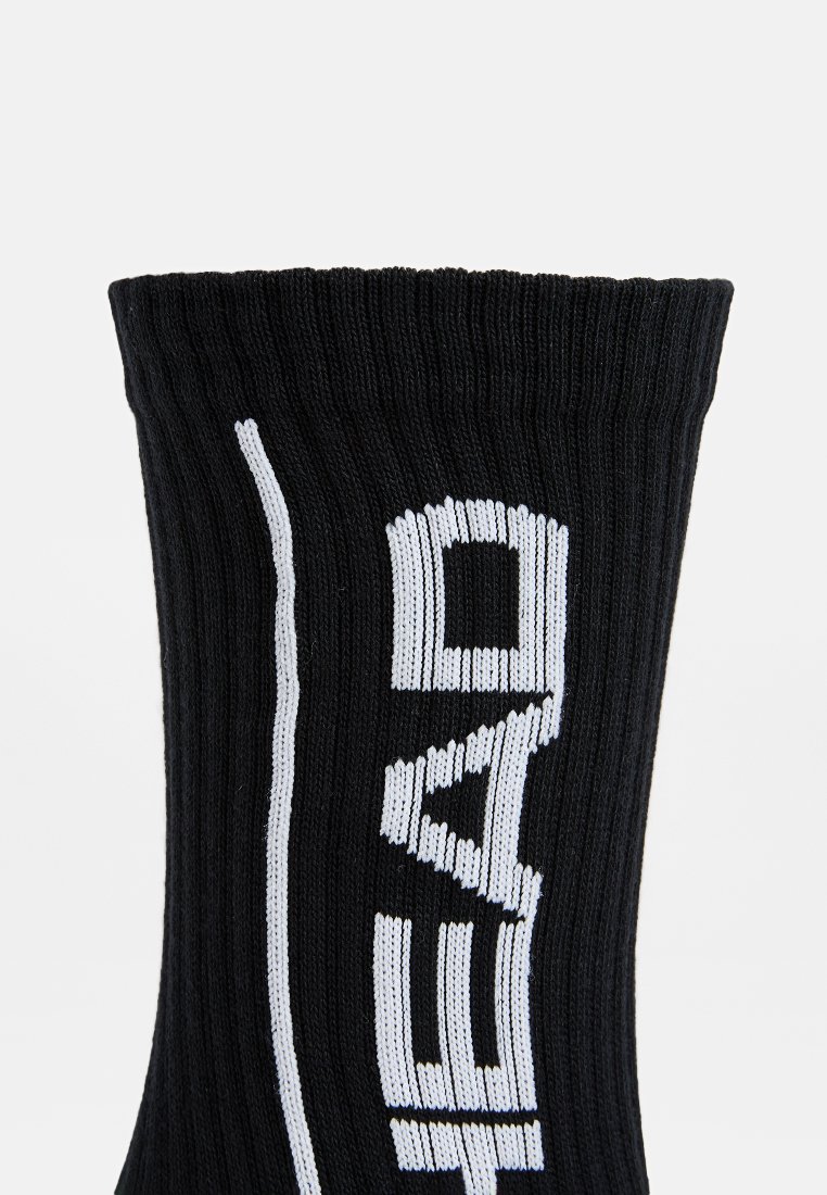 Calcetín negro de punto con textura acanalada, que presenta texto impreso en blanco en el lado y un puño ancho. Diseño elegante, sin adornos, centrado en la legibilidad.