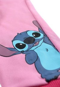 Tissu rose présentant un personnage de dessin animé aux grands yeux noirs, oreilles bleues et bras. Le personnage sourit en étendant les bras, avec une finition texturée.