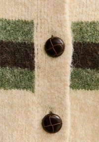 Cremefarbener Strickcardigan mit grünen und braunen Streifen, ausgestattet mit einem großen dunkelbraunen Knopf mit einem Kreuzdesign. Weiche Textur.