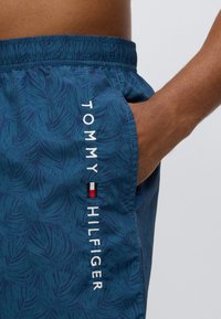 Μαγιό σορτς σε σκούρο μπλε με σχέδιο φύλλου, με λευκό κεντητό λογότυπο στο πλάι και ελαστική μέση για άνεση.