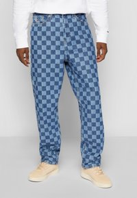 Modré kostkované džíny s volným střihem, se zipem, poutky na opasek a jemným vyblednutím. Doplněné béžovými teniskami.