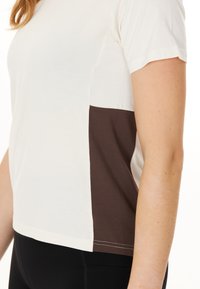 Kortärmad t-shirt i krämfärgad framdel och brun sidopanel, gjord av mjukt tyg med rak passform och kontrasterande sömmar.