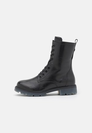 Botte chelsea en cuir noir avec de multiples œillets, devant lacé, col rembourré et semelle en caoutchouc épaisse avec une légère teinte bleue.