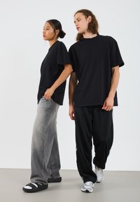 T-shirts noirs surdimensionnés, en tissu de coton, coupe décontractée. Jeans gris à jambes larges, texturés. Pantalons foncés avec logo, chaussures de sport. Design simple.