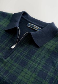 Marineblaues und grünes karriertes Polohemd mit Reißverschluss, aus Strickstoff und mit weichem Kragen. Das Etikett trägt den Schriftzug "ZYX Premium Collection".