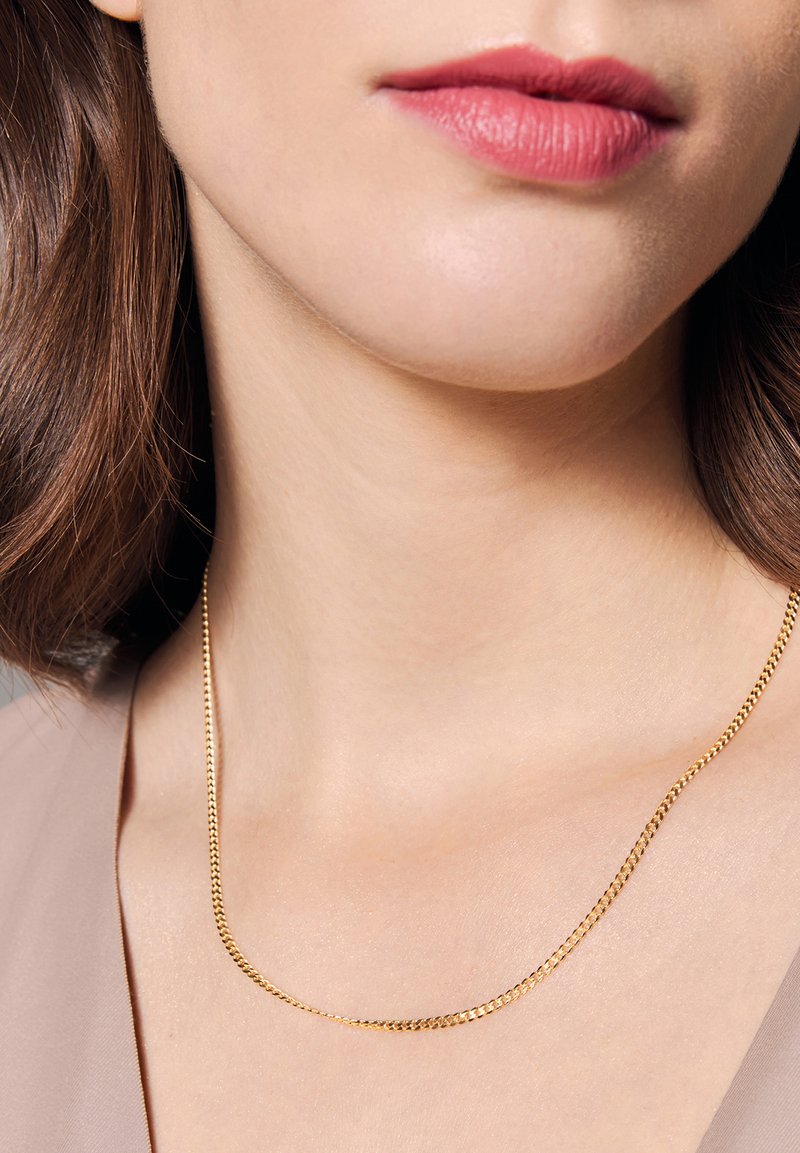 Złoty metalowy naszyjnik łańcuszkowy o gładkim, płaskim designie, spoczywający na szyi. Łańcuszek ma subtelną teksturę i lekki połysk.