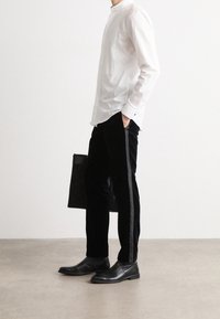 Biała, longsleeve koszula z plisami i stójką, połączona z czarnymi, aksamitnymi spodniami z satynowymi paskami po bokach; eleganckie czarne botki.
