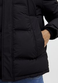 Black puffer jacket with a quilted design. Features a high collar, zippered front, and side pockets. Fabric appears smooth and slightly glossy.