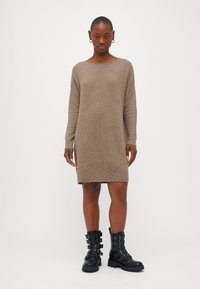 Vestido de malha em castanho claro, com mangas longas e gola redonda. Combinado com botas pretas até ao joelho com detalhes em metal prateado.