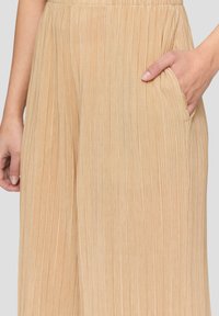 Beige plissierte weit geschnittene Hosen aus strukturiertem Stoff; mit einer Seitentasche. Der elastische Bund verbessert den Komfort und die Passform.